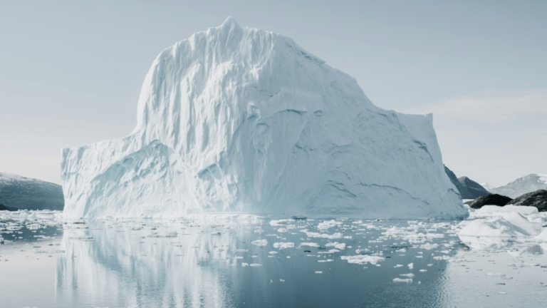 Large iceberg floating above and below the waterline, calm grey sea