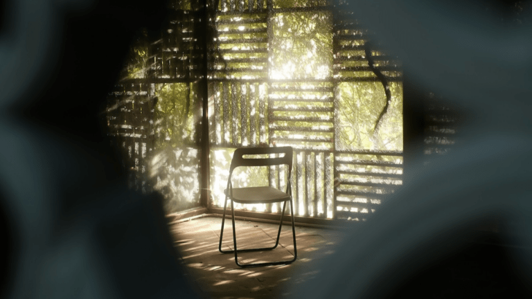 Empty folding chair in dappled sunlight on a wooden porch, green light filtering through