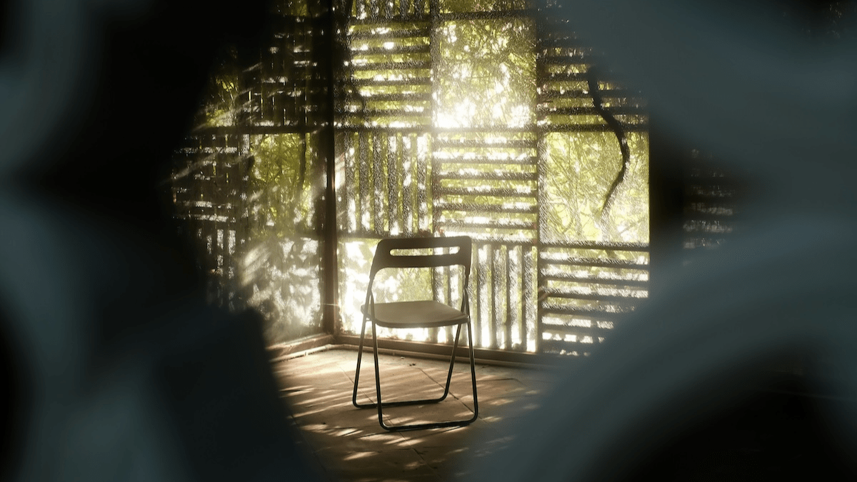 Empty folding chair in dappled sunlight on a wooden porch, green light filtering through