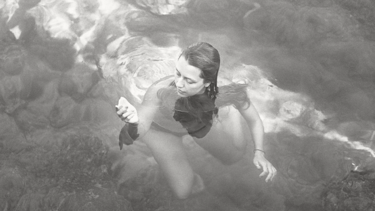 Woman floating underwater in dark water, partially submerged, representing mental load and emotional overwhelm.