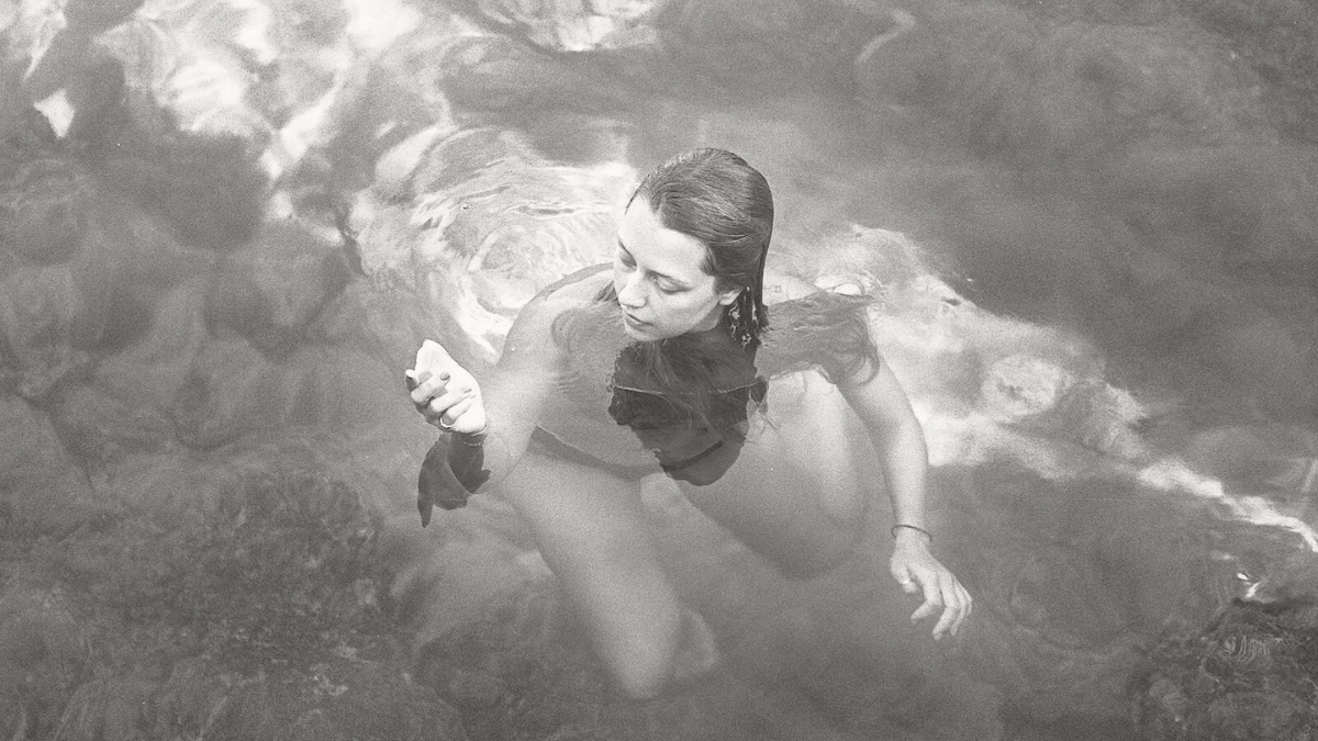 Woman floating underwater in dark water, partially submerged, representing mental load and emotional overwhelm.