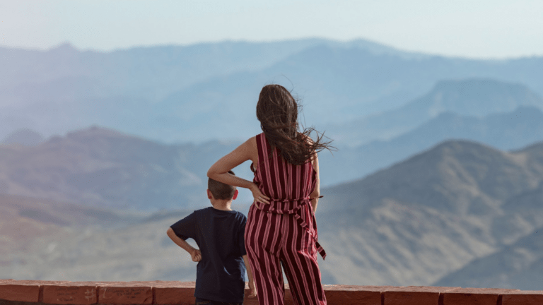 A woman and a child stand together, looking out at something ahead.