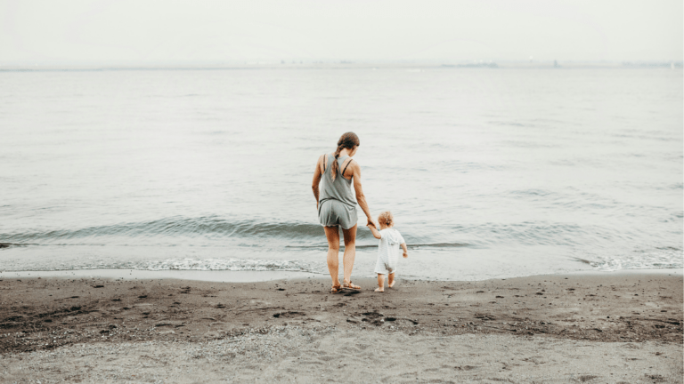 Mother guiding a young child toward the shoreline, hand in hand