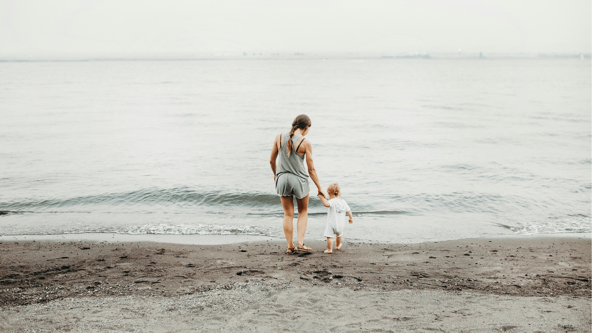 Mother guiding a young child toward the shoreline, hand in hand